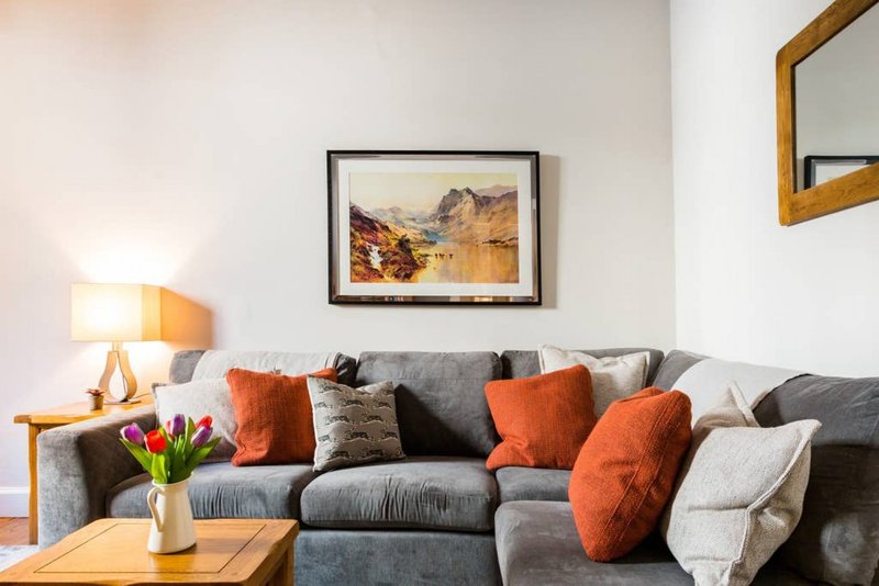 Modern living room with gray sofa, orange cushions, wooden coffee table, and framed landscape artwork