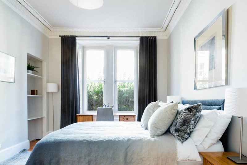 Bright modern bedroom with double bed, built-in shelving, French doors and dark curtains