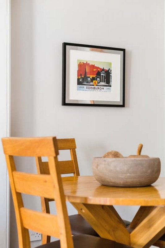 Wooden dining table with two chairs, framed artwork on white wall above