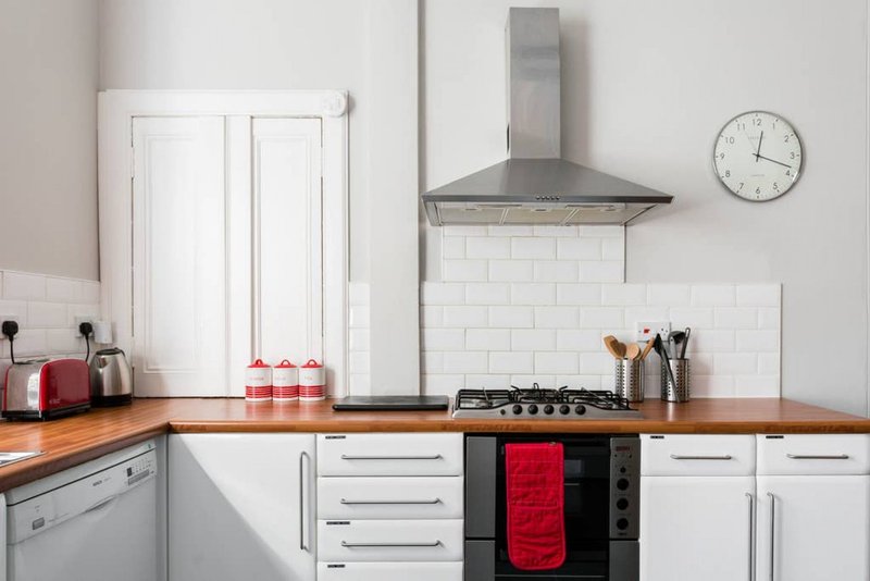 Modern kitchen with white cabinetry, wooden countertop, gas cooktop, stainless steel range hood and wall clock