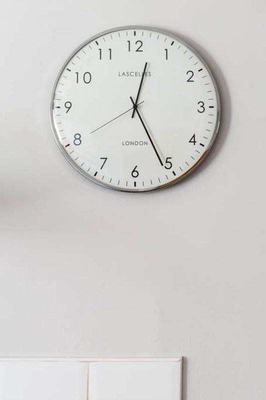 Wall-mounted round clock with gray frame showing time, above white wall and door frame