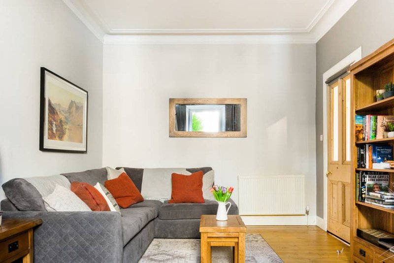 Living room with gray corner sofa, orange cushions, wooden shelving unit and framed wall art