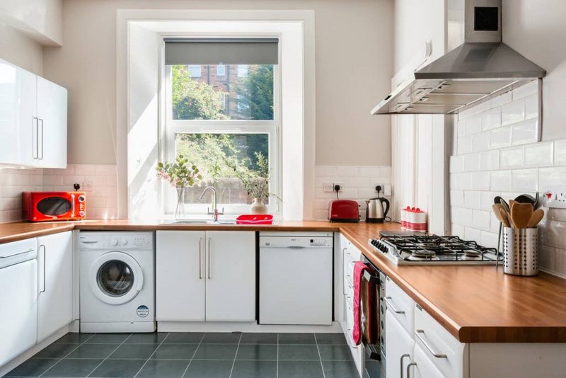 Modern kitchen with white cabinetry, wooden countertops, gas hob, and large window overlooking garden