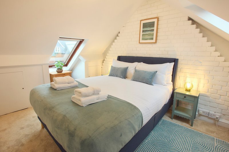 Bright attic bedroom with double bed, skylight window, white brick walls and wooden flooring