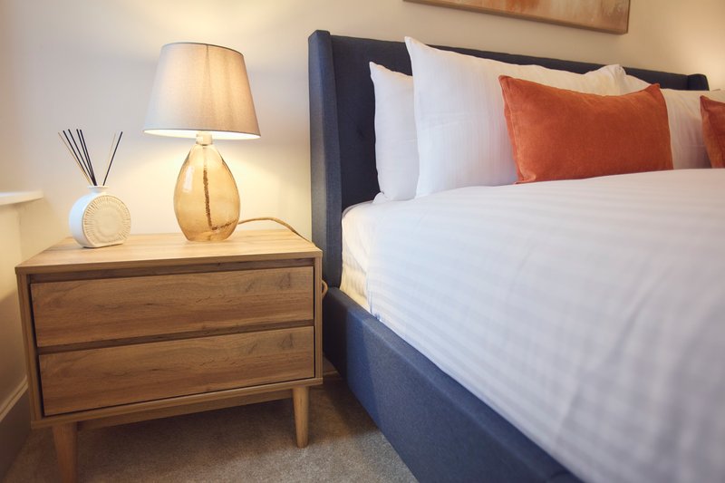Bedroom with double bed, wooden nightstand, table lamp and orange accent pillows