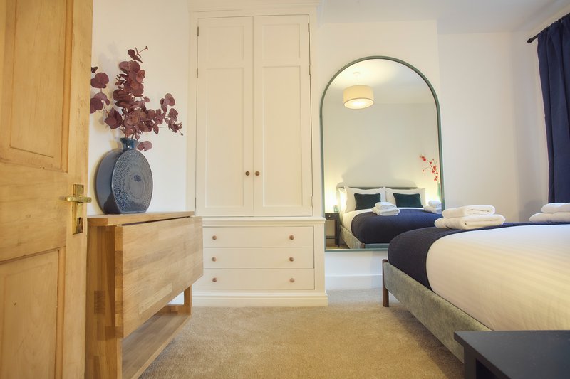 Bright bedroom with two beds, wooden furniture, arched mirror, and dried flowers in vase