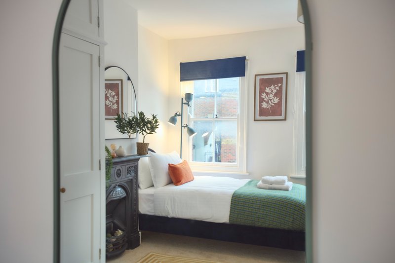 Bright bedroom with double bed, green throw, window with blue blind, and framed wall art