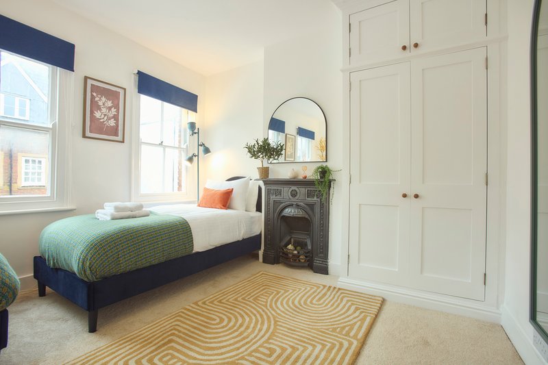 Bright bedroom with single bed, fireplace, wardrobe and geometric patterned rug
