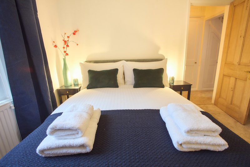 Bedroom with double bed, white pillows, folded towels, dark runner, and bedside tables