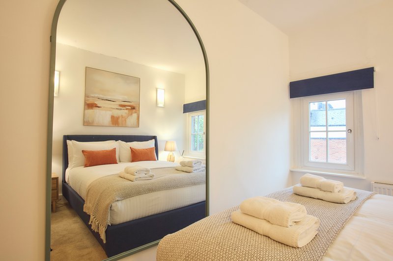 Bright bedroom with canopy bed, single bed, arched mirror, and window with navy trim