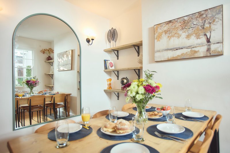 Dining room with wooden table set for four, arched mirror, shelving, and framed wall art