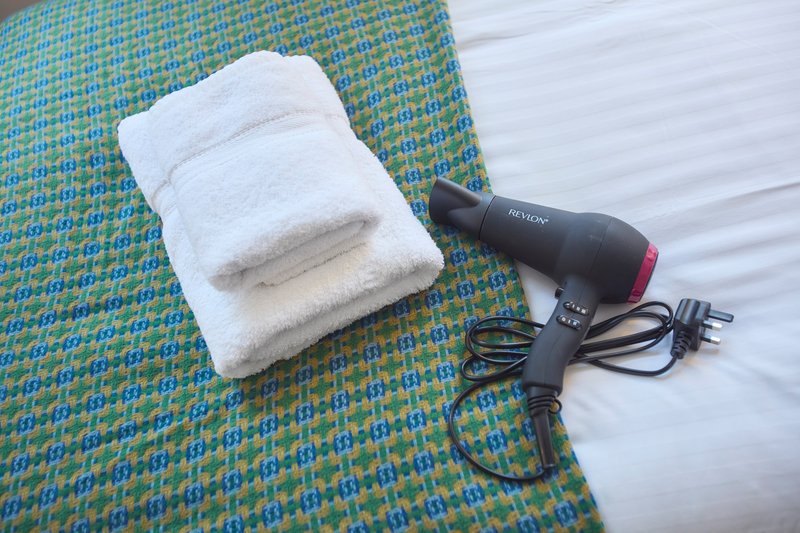 Folded white towels and hair dryer on patterned bedspread