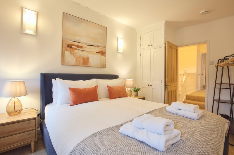 Bright modern bedroom with double bed, orange accent pillows, wooden nightstand and warm lighting