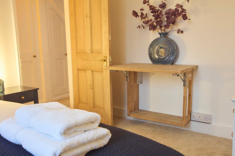 Bedroom with wooden wardrobe, console table, dried flowers in vase, and folded towels on bed