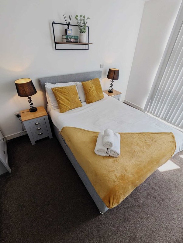 Modern bedroom with double bed, yellow cushions, bedside tables, lamps and wall-mounted shelf