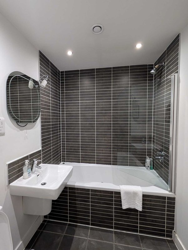 Modern bathroom with black tile walls, white sink, bathtub and round mirror