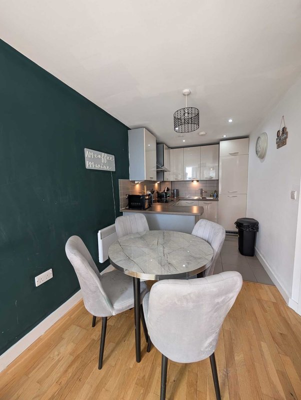 Open-plan kitchen and dining area with round marble table, grey chairs and dark green accent wall