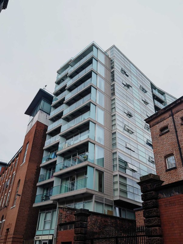 Modern apartment building exterior with multiple balconies, glass and metal facade, adjacent brick buildings