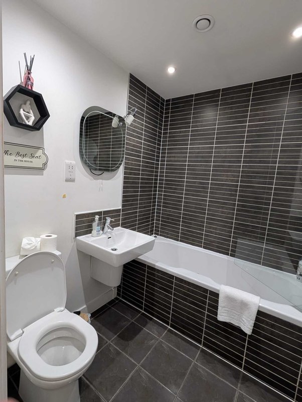 Modern bathroom with black tile walls, white toilet, sink and bathtub with towel rail