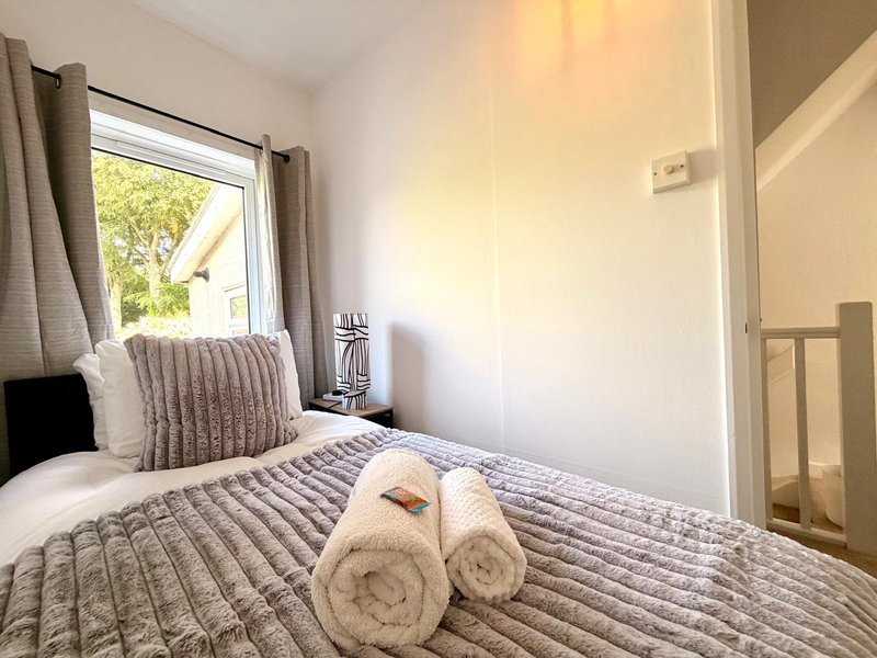Bright bedroom with double bed, rolled towels, cushions, window with garden view