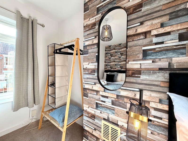 Bedroom with wooden accent wall, mirror, clothes rack, window with curtains and bed