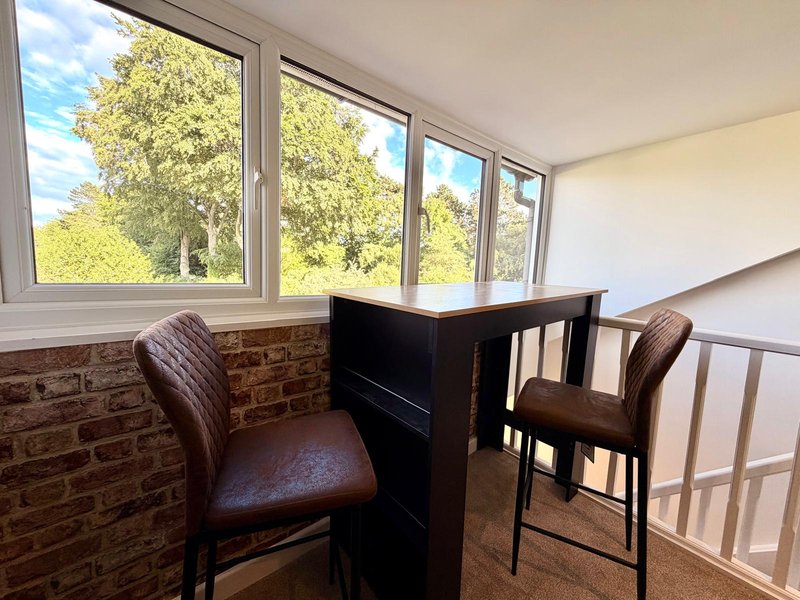 Sunlit corner seating area with bar counter, leather stools, and large windows overlooking trees