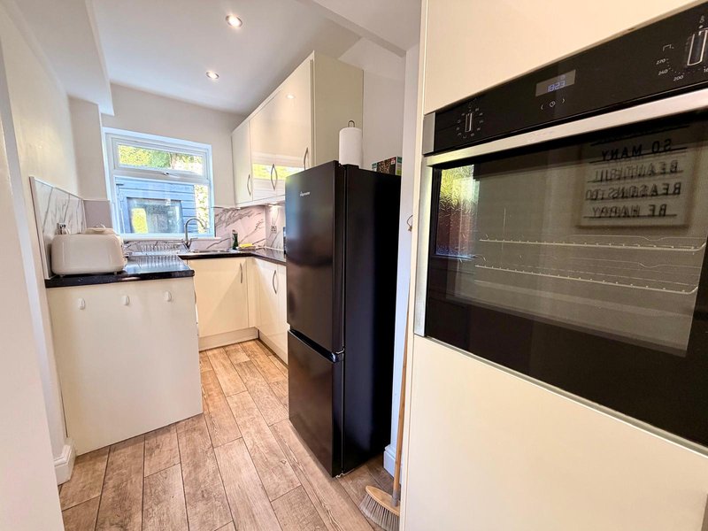 Compact kitchen with cream cabinetry, black fridge, built-in oven and wooden flooring