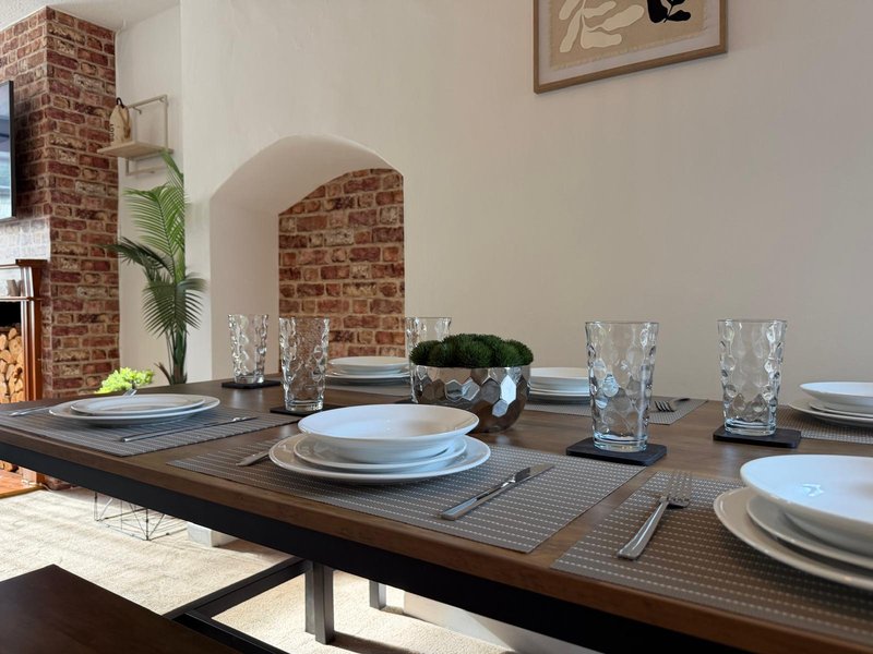 Dining table set for multiple guests with place settings, glasses, and potted plant centerpiece