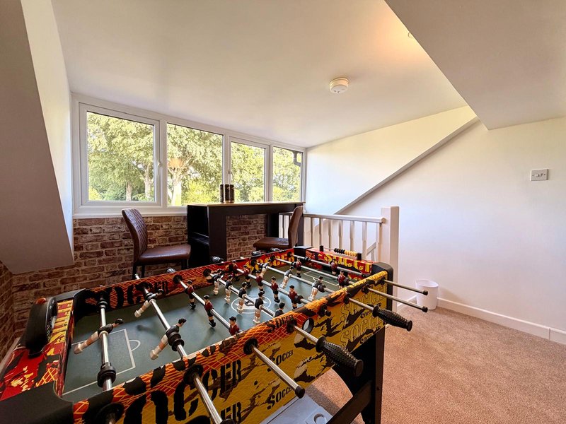 Bright attic room with foosball table, brick wall, large windows and wooden staircase