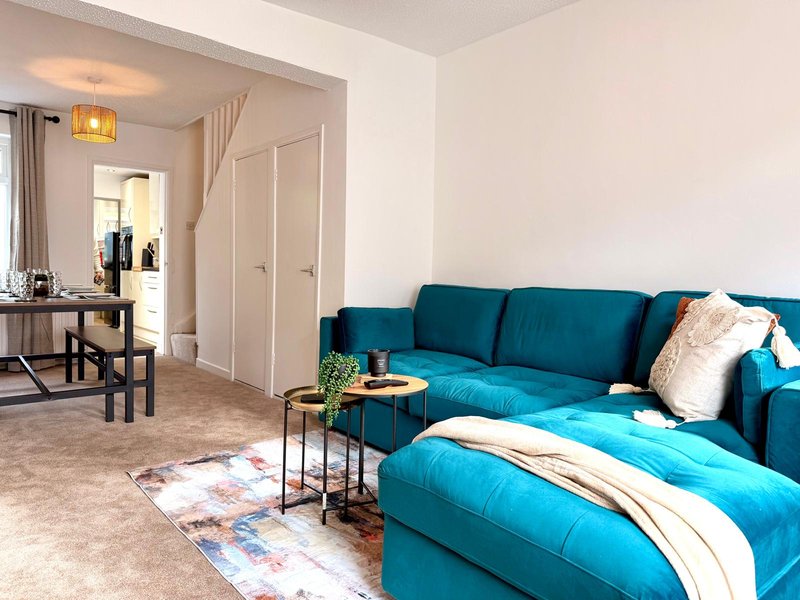 Open-plan living area with teal corner sofa, side tables, colorful rug, and dining space beyond