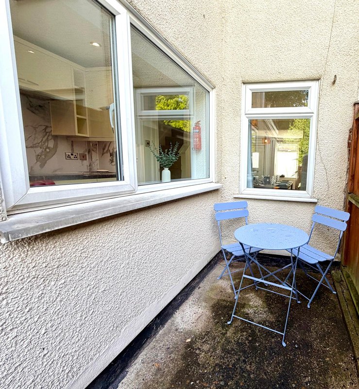 Exterior patio area with blue folding table and chairs, cream rendered walls