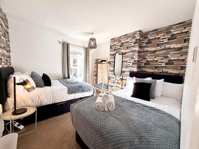 Bright twin-bedroom with two beds, brick feature wall, wooden flooring and modern furnishings