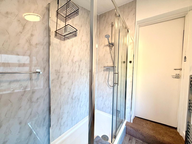 Modern bathroom with marble-tiled walk-in shower, hanging storage baskets and white door