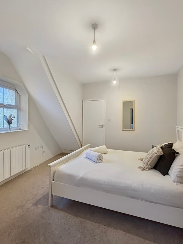 Bright attic bedroom with white bed, sloped ceiling, window, and pendant lights