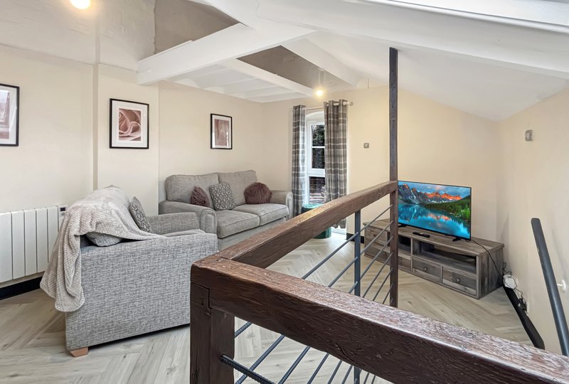 Open-plan living area with grey sofa, wooden staircase, TV, and framed wall art