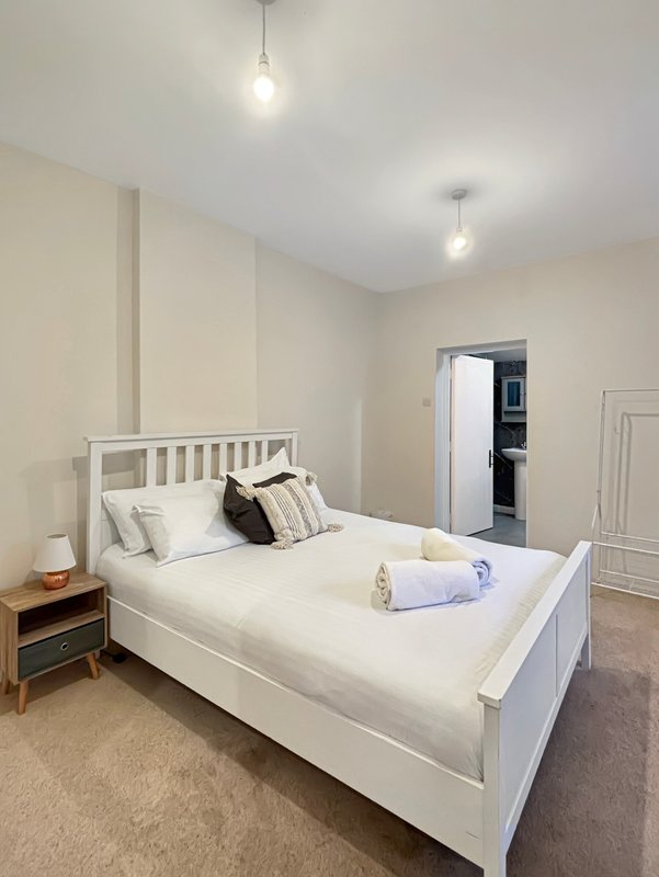 Bright bedroom with white bed, pendant lights, bedside table, and wardrobe