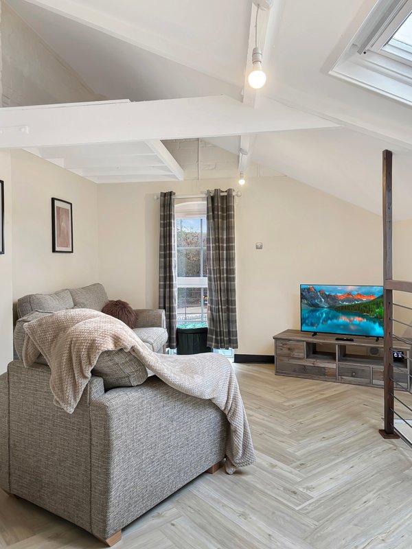 Modern attic bedroom with armchair, TV unit, herringbone flooring and skylights