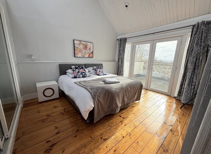 Bright bedroom with double bed, wooden floor, patio doors and countryside view