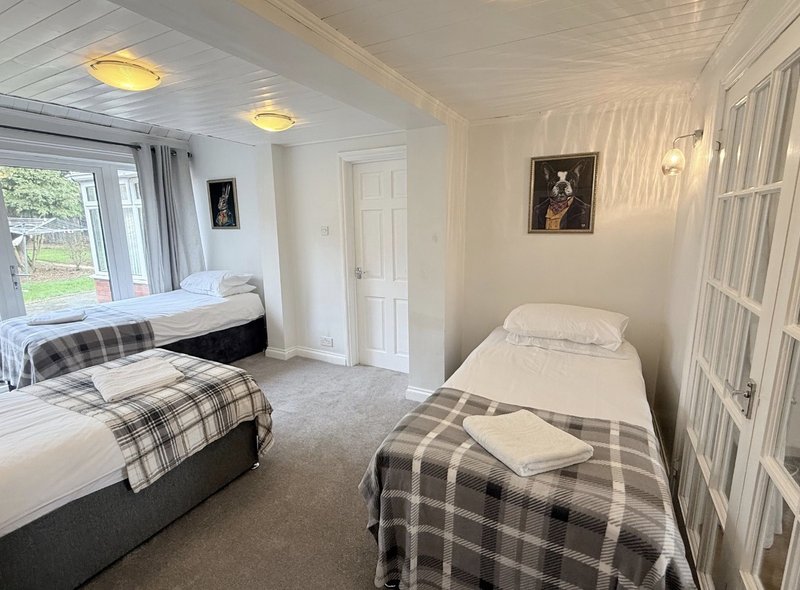 Bright bedroom with three single beds, plaid bedding, wooden doors and window with garden view