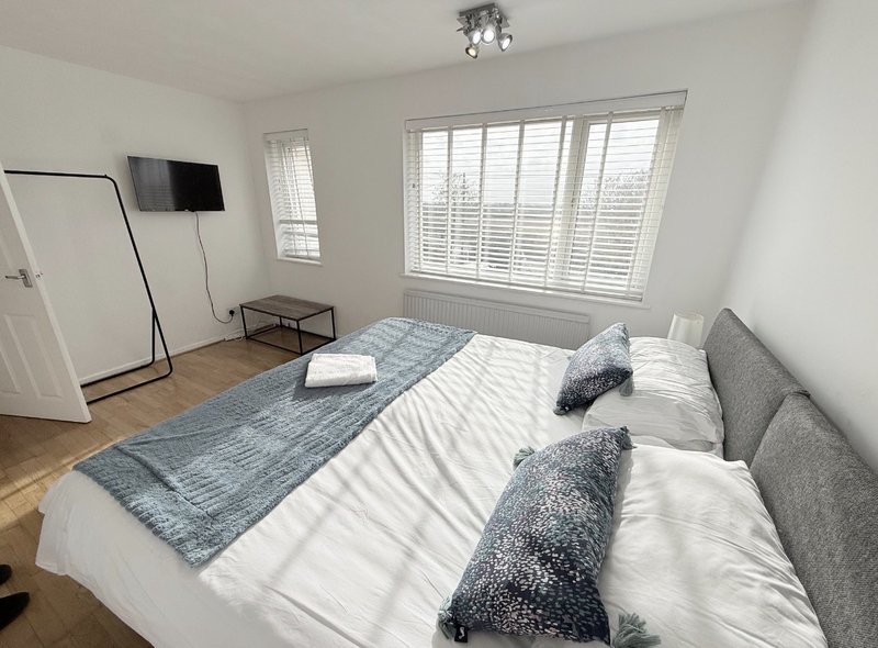 Bright bedroom with double bed, grey cushions, wooden floor, wall-mounted TV and shuttered windows