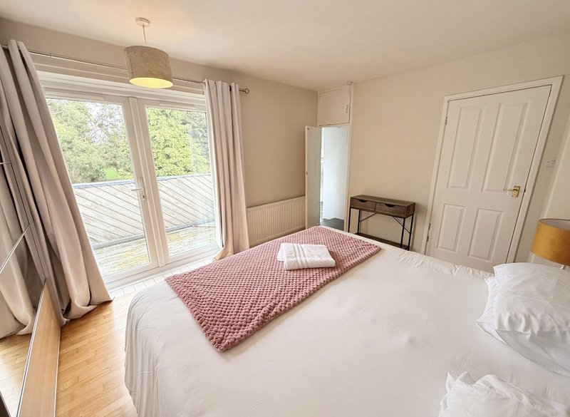 Bright bedroom with double bed, pink throw blanket, wooden floor and glass doors to balcony