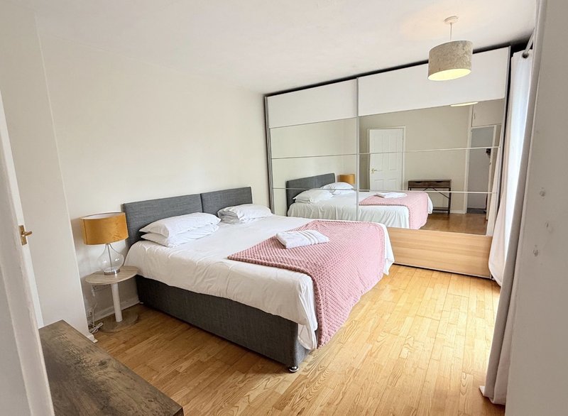 Bright bedroom with double bed, pink bedding, wooden floor and large mirror wardrobe