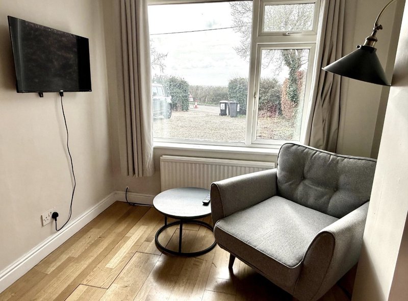 Living room with gray armchair, small round table, wall-mounted TV, and large windows overlooking garden