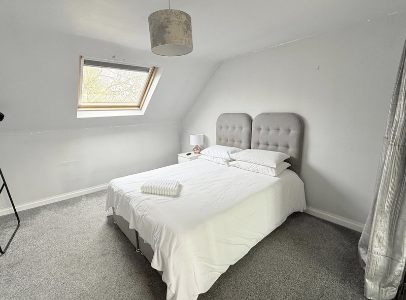 Bright attic bedroom with double bed, grey headboard, skylight window and pendant light