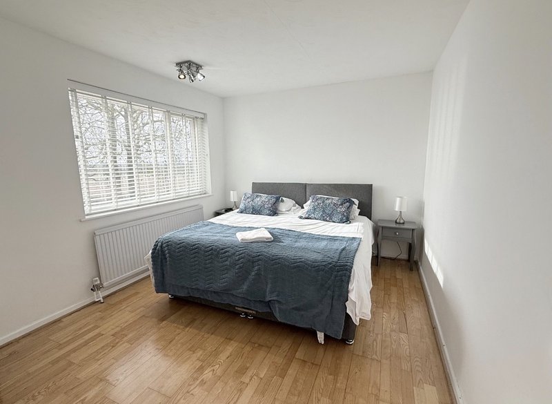 Bright bedroom with double bed, wooden floor, white walls and shuttered window