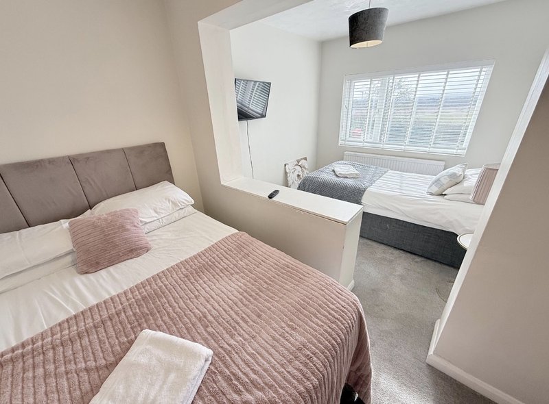 Modern bedroom with grey upholstered headboard, layered bedding, and window seat area with storage