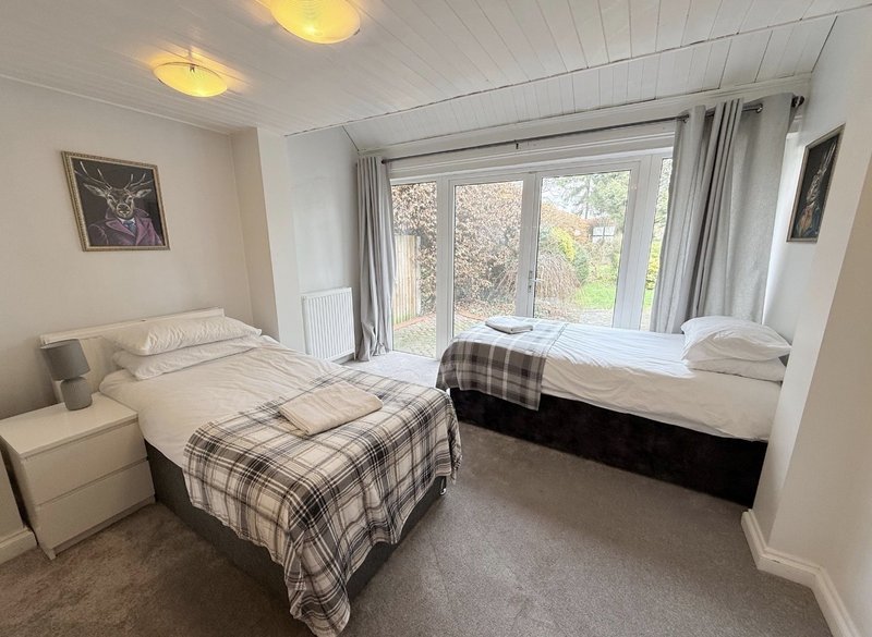 Bright bedroom with two single beds, plaid bedding, large windows overlooking garden