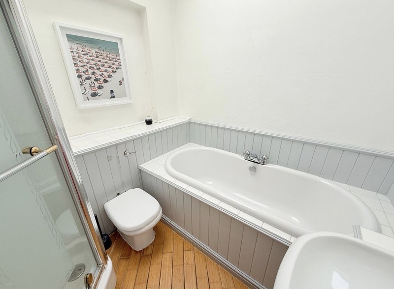 Modern bathroom with white suite, wooden floor, gray paneling and framed wall art