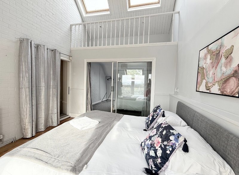 Bright modern bedroom with double bed, gray headboard, mezzanine loft above, and glass doors to balcony