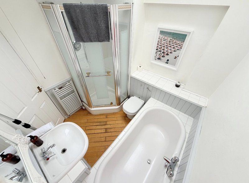 Bright bathroom with white walls, wooden floor, sink, bathtub and shower cubicle